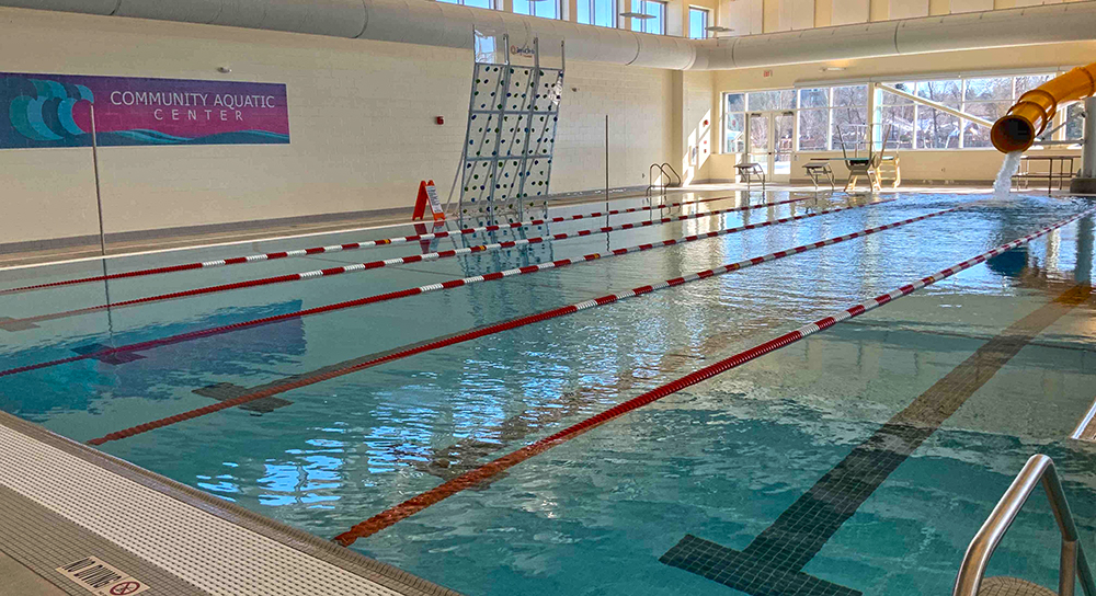 Indoor lap pool with a climbing wall, water slide, diving board, and starting blocks at the Sheridan YMCA